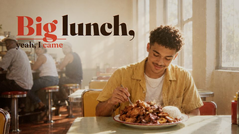 A young man tucks into lunch in a sunlit diner, under the line “Big lunch, yeah, I came”